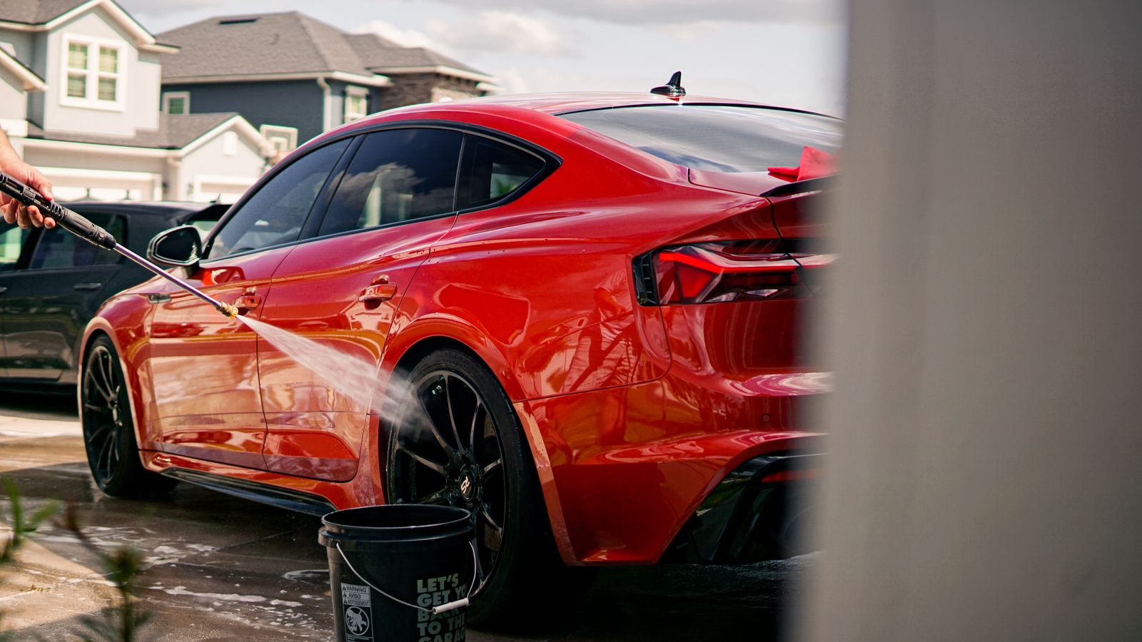 Rinsing a red sedan in a customer's driveway — after